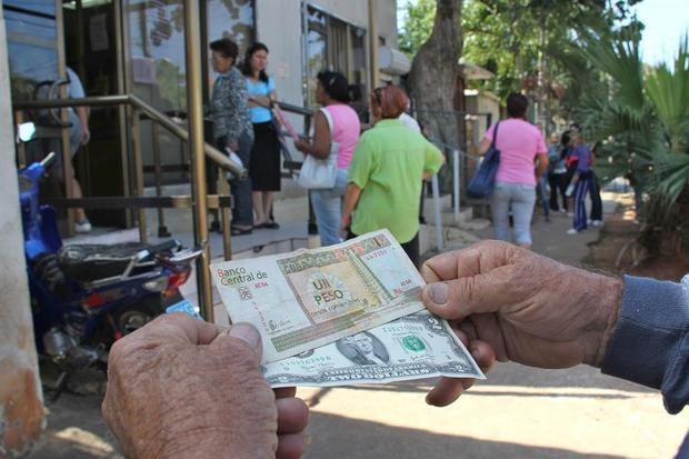 Un hombre muestra un peso convertible cubano y un dólar estadounidense.