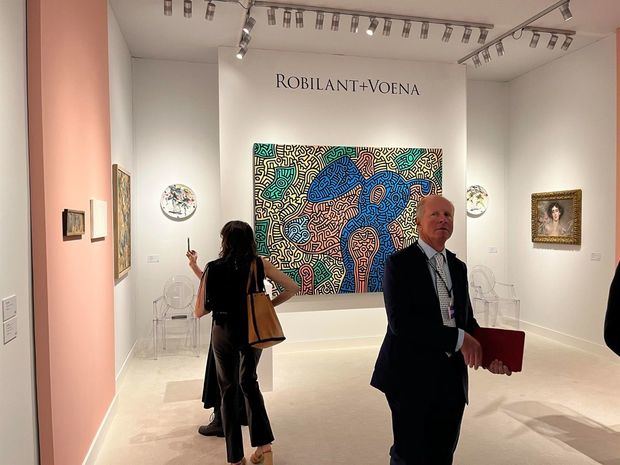 Personas observan obras expuestas en el espacio de la galería Robilant+Voena frente a la obra 'Piglet goes shopping' -'Cerdita se va de compras'- (1989) de Keith Haring, durante una presentación previa de la feria TEFAF, este 5 de mayo de 2022.