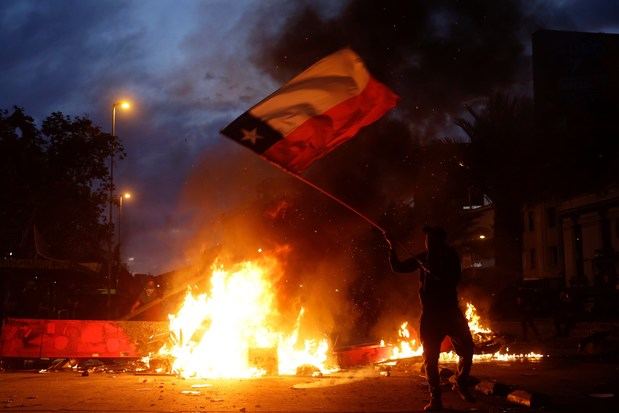 Un manifestante fue registrado este viernes al protestar, en medio del fuego e izando la bandera de Chile, para pedir la renuncia del presidente chileno, Sebastián Piñera, en Santiago de Chile.