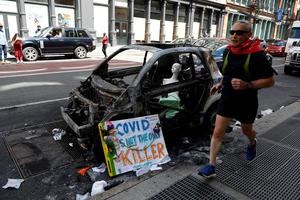 Un hombre trota junto a un auto quemado del Departamento de Policía de la ciudad de Nueva York frente a la tienda de Bloomingdale's en SOHO después de las últimas noches saqueando disturbios como parte de la respuesta de los manifestantes a la muerte de George Floyd, en Nueva York, Nueva York, EE. UU.