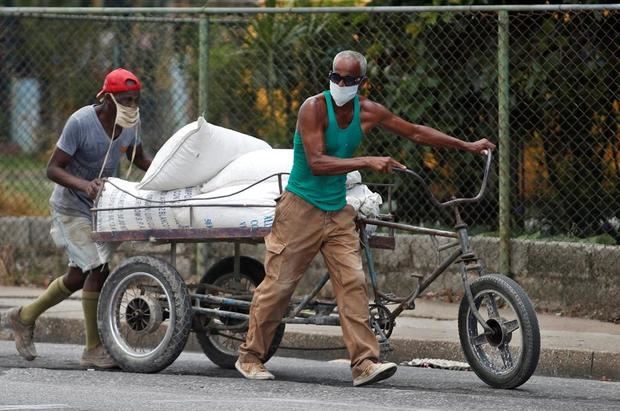 Dos hombres con mascarillas empujan un triciclo con carga por una calle, en La Habana, Cuba.