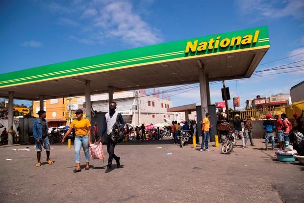 Ciudadanos fueron registrados este domingo al caminar por una estación de suministro de gasolina, que no está prestando servicio al público, en Puerto Príncipe, Haití.