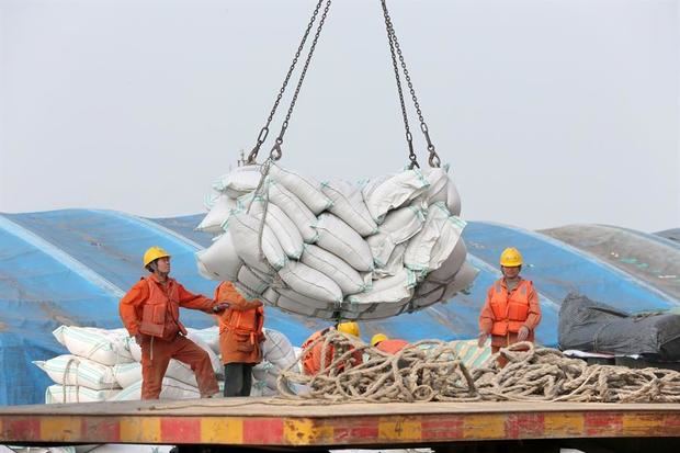 Fotografía de unos operarios mientras transportan bolsas de habas de soja en un puerto en Nantong, China.