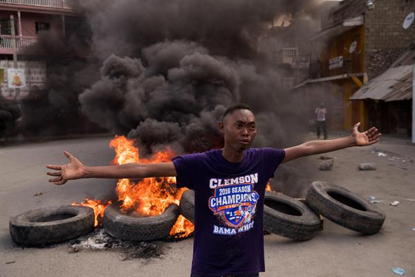 Un hombre camina frente a una pila de llantas en llamas durante una jornada de protestas a la vez que se rindieron homenajes al asesinado presidente Jovenel Moise, 