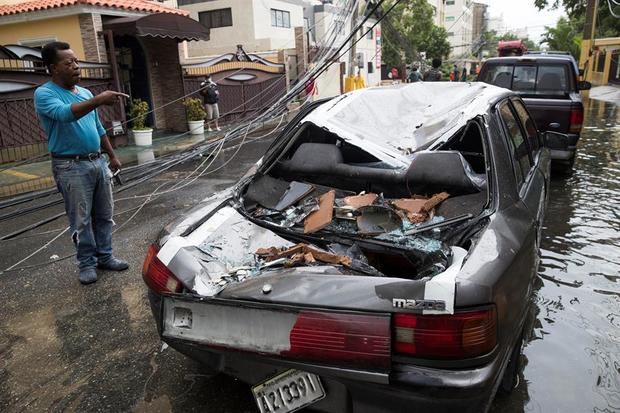 Un hombre observa su automóvil que resultó aplastado por un poste de alumbrado eléctrico debido a las intensas lluvias de la tormenta Laura, este domingo en Santo Domingo (República Dominicana). 
