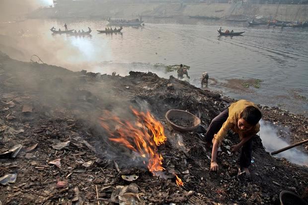 Fotografía cedida por el Fondo de las Naciones Unidas para la Infancia (Unicef) donde aparece un niño quemando basura mientras está parado sobre un montón de escombros a orillas del río Buriganga, en Hazaribagh, un subdistrito del distrito central de Dhaka, Bangladés.