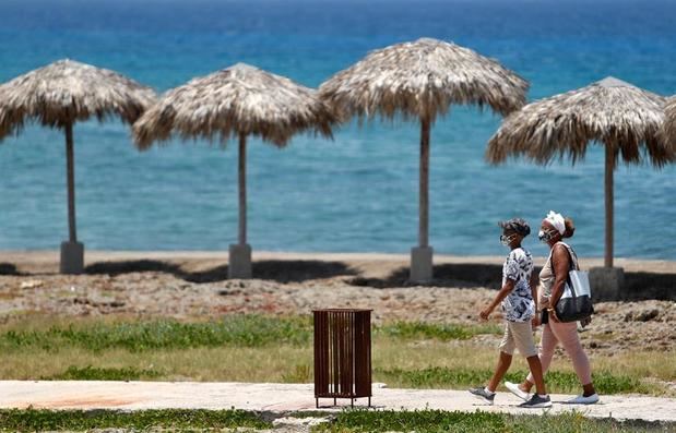 Dos personas con tapabocas caminan frente al mar , en La Habana, Cuba.
