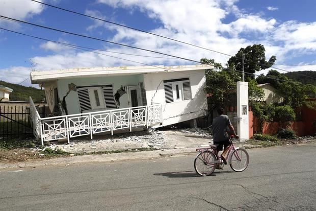 Una persona en bicicleta pasa delante de una casa dañada por el temblor de magnitud 5,8 que se reportó este lunes a las 06.32 hora local (10.32 GMT) en la costa de Guánica, municipio del suroeste de Puerto Rico.