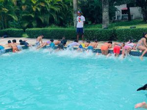 Niños ejercitándose en la piscina junto a entrenador.