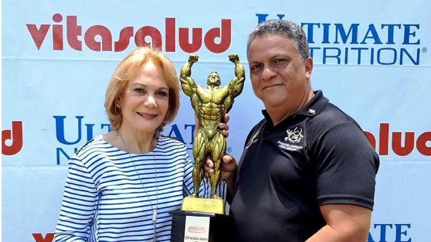 Doña Clara Cabrera y Tony Peña R, exhiben la gran copa Vitasalud que se disputará en el gran absoluto del campeonato nacional Mister República Dominicana de fisiculturismo y fitness para novatos.