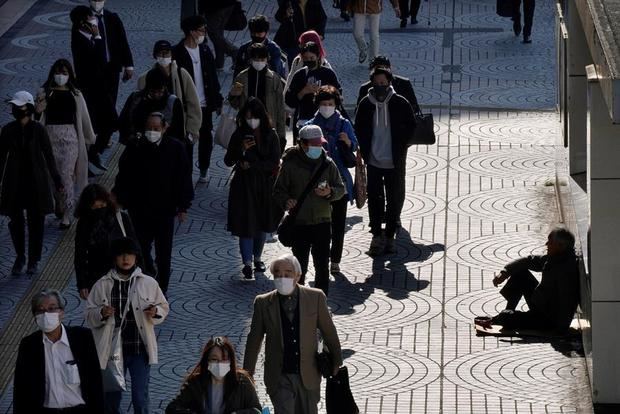 Los peatones pasan junto a una persona sin hogar (d) sentada con una lata en el distrito de negocios de Shinjuku en Tokio, Japón.