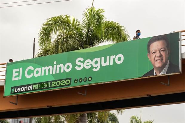 Una mujer con tapabocas es vista mientras pasa cerca a una valla publicitaria del candidato presidencial Leonel Fernández, este sábado en Santo Domingo.