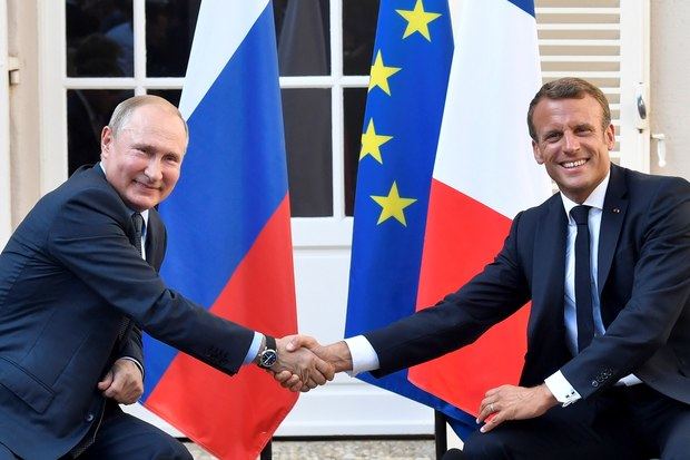 Vladimir Putin y Emmanuel Macron se saludan ante las banderas de Rusia, Francia y la Unión Europea.