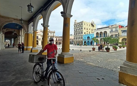 Fotografía de archivo en donde se ve a un hombre que camina con su bicicleta por los portales de una plaza en Cuba. 