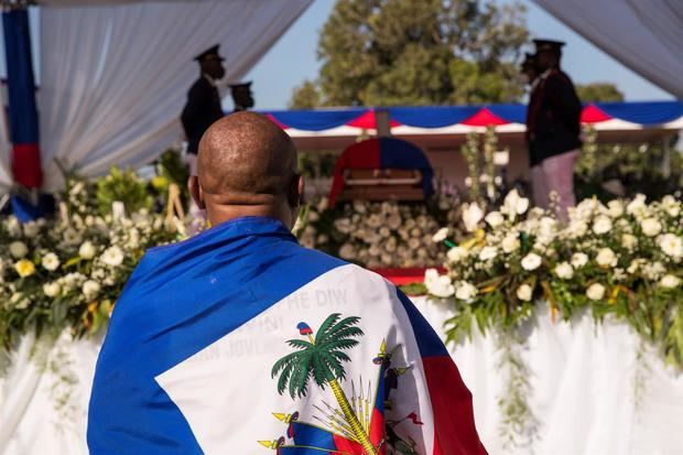 Un hombre envuelto con la bandera nacional observa el féretro del presidente Jovenel Moise, durante su ceremonia fúnebre.