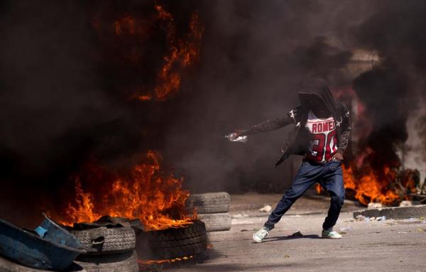 Un manifestante aviva el fuego de una barricada de llantas en llamas en la zona próxima al aeropuerto internacional de Puerto Príncipe (Haití). 