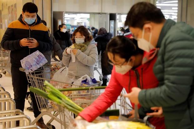 Varios clientes con máscaras protectoras y gafas revisan su factura después de comprar comestibles en un supermercado en un centro comercial en Pekín, China. 