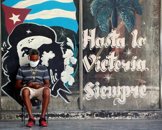 Un hombre con tapabocas revisa en su celular, junto a un graffitis con la imagen del guerrillero argentino-cubano Ernesto “Che” Guevara en La Habana (Cuba). Imagen de archivo.